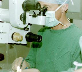 surgeon operating whilst looking through mobile microscope
