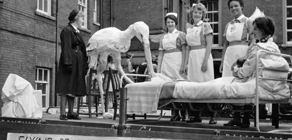 Model stork with mother in bed and maternity staff on back of carnival float