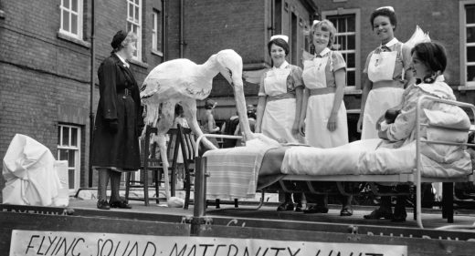 Model stork with mother in bed and maternity staff on back of carnival float