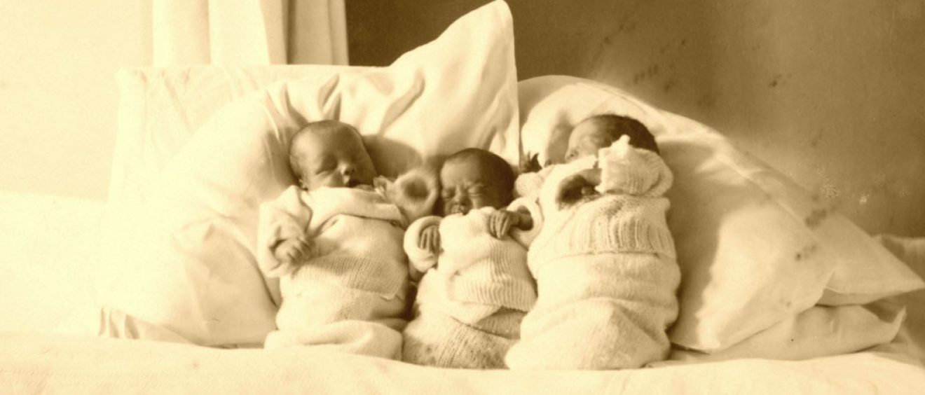 Three babies wrapped up in blankets and propped up pillows