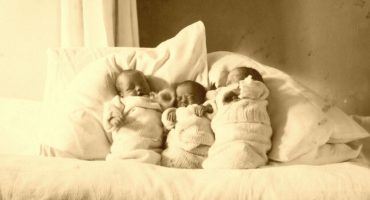 Three babies wrapped up in blankets and propped up pillows