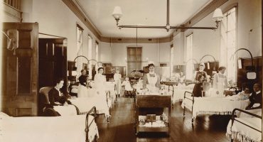 Nurse pushing drug trolley between beds on ward