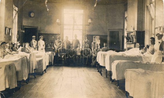 Patients in beds either side of ward and seated at the end with nurses