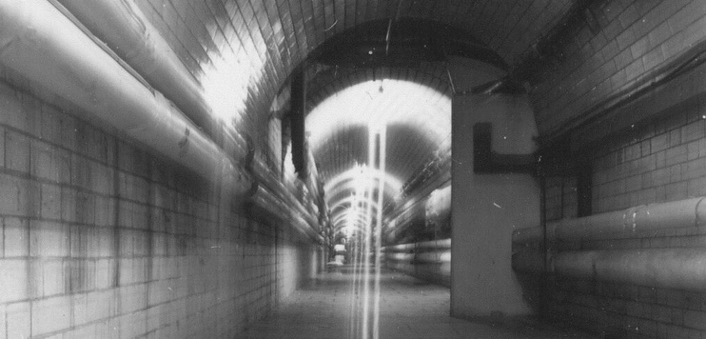 Black and white photo of tunnel with tiles and pipes