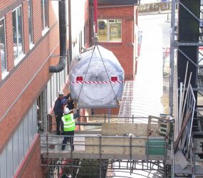 MRI scanner on end of crane hook about to enter the side of hospital building