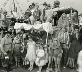 Staff and children dressed as pirates and other characters stand next to float