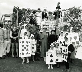 Children in playing card costumes, staff as Mad Hatter, white rabbit etc.. stand next to float
