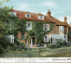 large brick house with tile roof, conservatory on front and ivy growing up, lawn in front and trees in garden