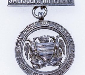 silver metal badge with Salisbury city crest and Infirmary motto