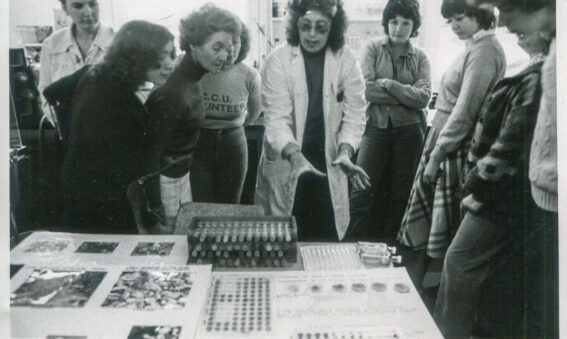 black and white photograph of group of people looking at science experiment