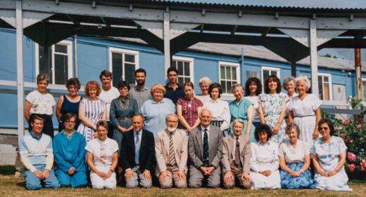 colour photograph of a group of staff in 2 rows in front of blue building