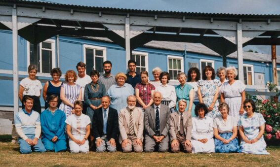 colour photograph of a group of staff in 2 rows in front of blue building