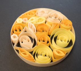 coiled strips of paper in varying shades of yellow clustered together inside a larger paper circle