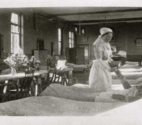 Nurse handing drink or medication to soldier on ward, flowers on central table