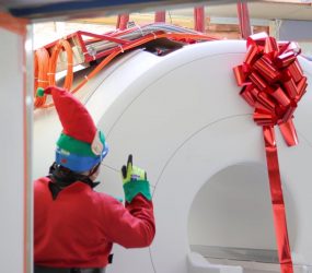 man dressed as elf oversees delivery of MRI scanner wrapped with giant red bow