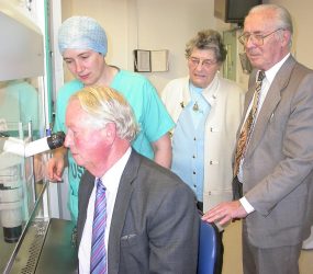 man looks through powerful microscope with staff member looking on