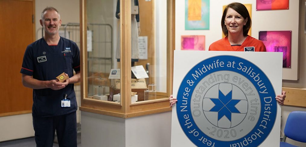 Lorna holding large badge design print out, standing next to display cabinet with Henry