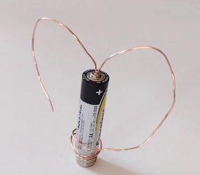 copper wire coiled into heart shape around AA battery balanced on two magnets