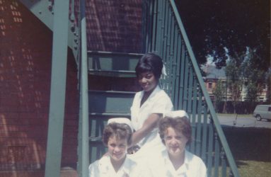 Three student nurses in uniform sitting on metal steps of nurses home
