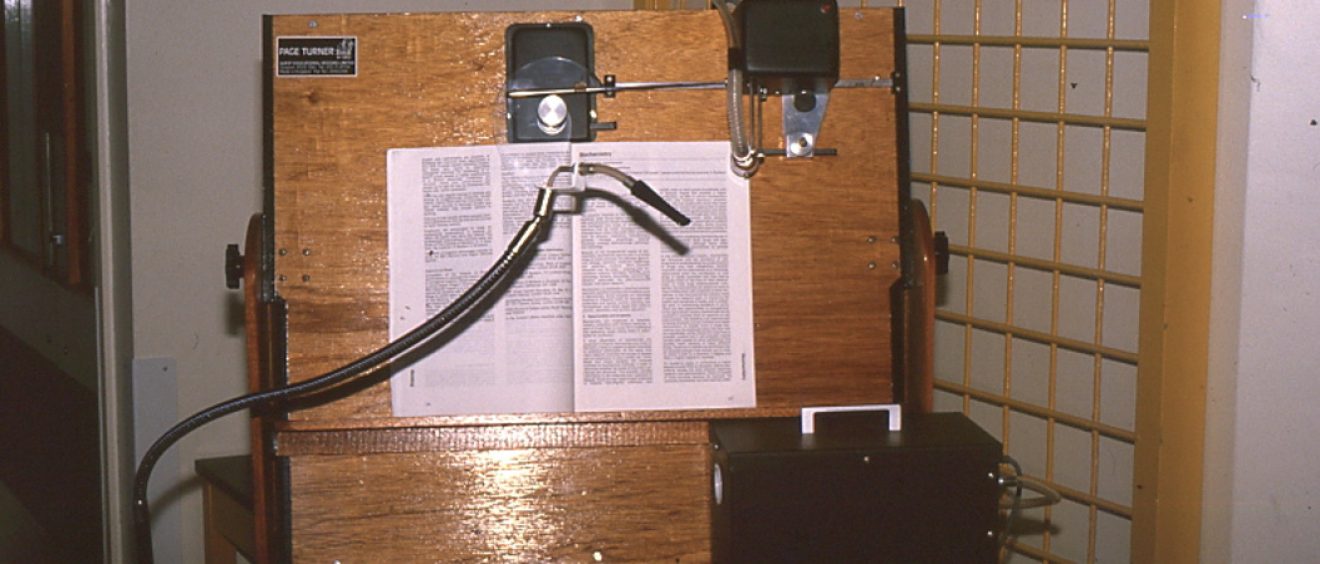 large wooden board holding a text book with tube attachment and device to turn the page