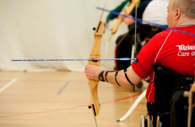 man in wheelchair drawing back bow preparing to shoot an arrow