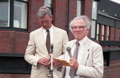 two men standing behind microphone, in front of the Spinal Unit building